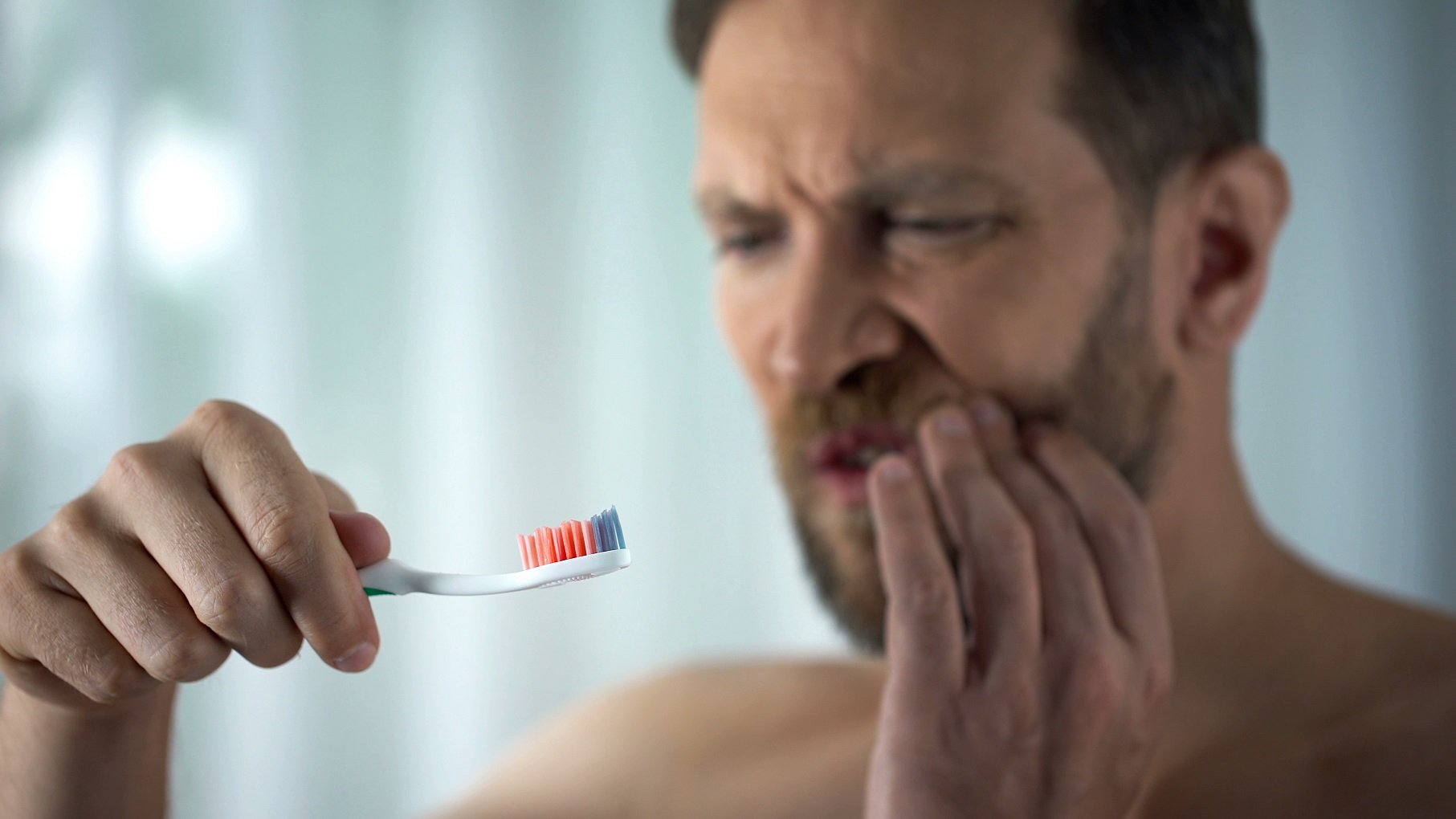 tooth decay symptoms True Dental man experiencing mouth soreness while looking at toothbrush