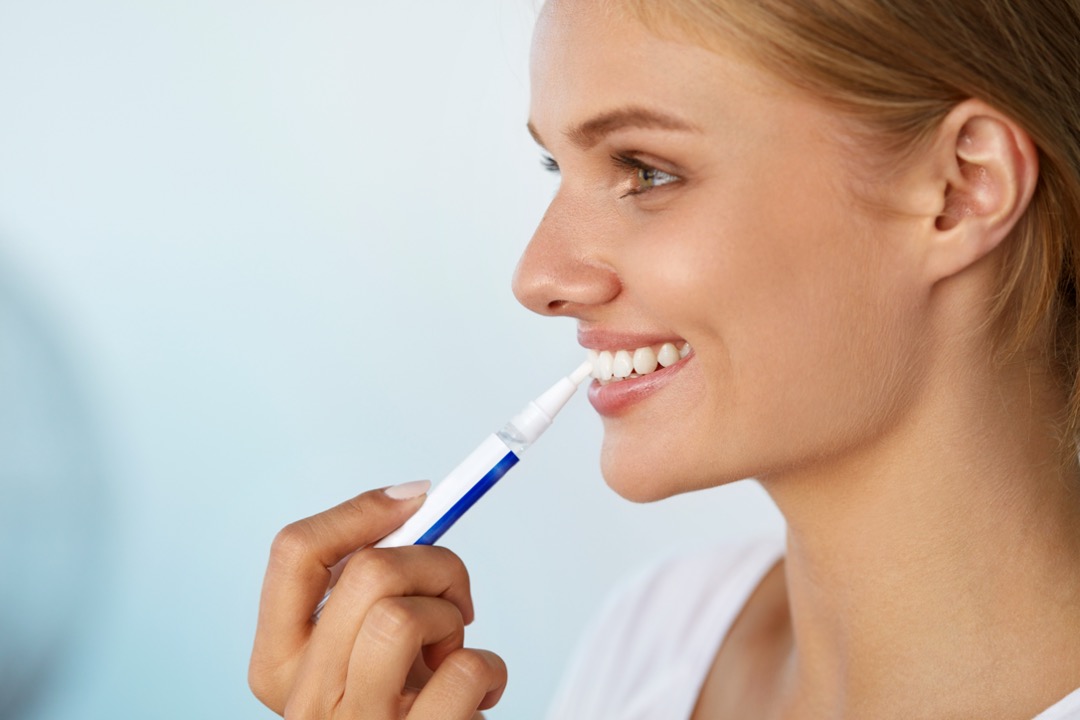 Woman whitening her teeth with a whitening pen